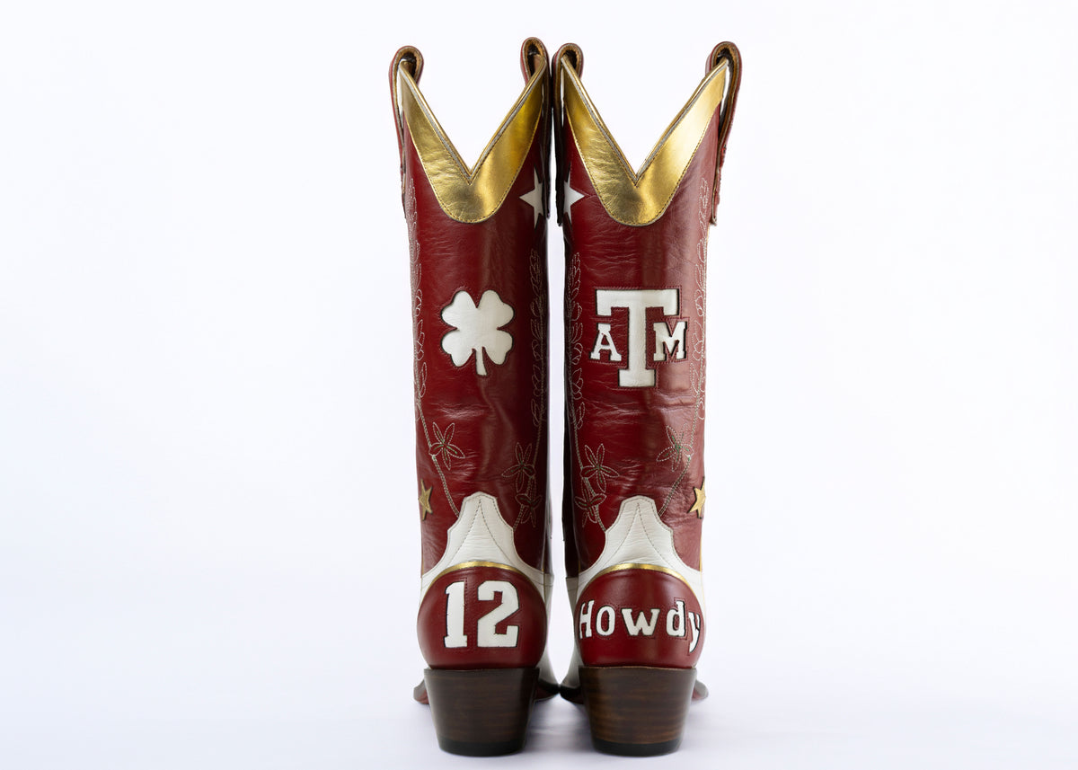A pair of custom red leather cowboy boots with gold trim, featuring Texas A&M University branding, a white shamrock, and the number 12, shown from the back against a white background.